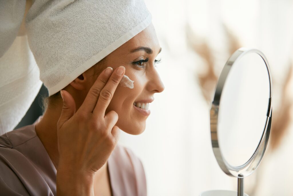 Woman applying a retinal night cream as part of a routine featuring a vitamin C serum in Australia and active skincare products to support collagen.